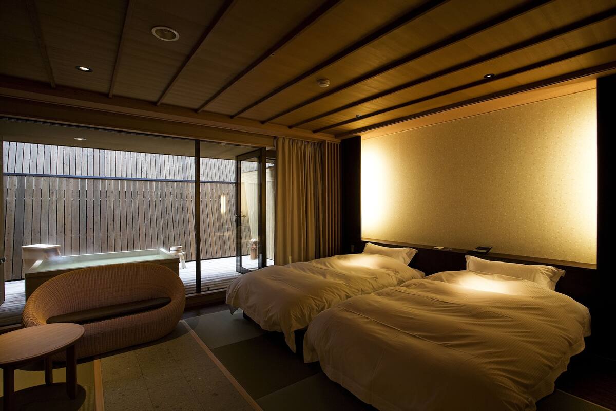 Een hotelkamer met twee bedden, een zithoek en uitzicht door een groot raam.