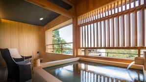 Interior de madera con un jacuzzi, una silla y una ventana con persianas verticales.