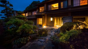Una casa tradicional japonesa con un sendero de piedra que conduce a la entrada, rodeada de abundante vegetación.