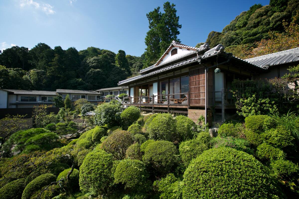 Een traditioneel Japans gebouw met een houten constructie en pannendak, omringd door weelderig groen en heuvels.