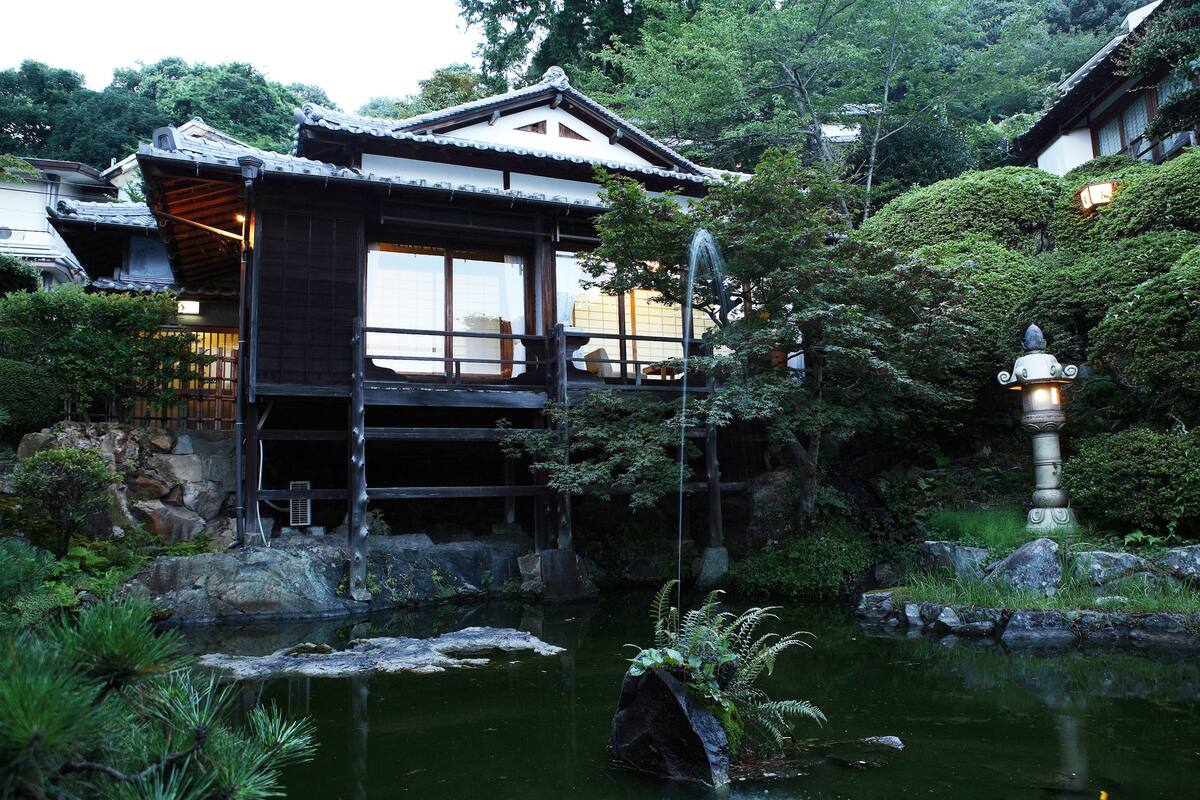 Een traditioneel Japans gebouw met een houten gevel en grote ramen, omgeven door een vijver en weelderige begroeiing.