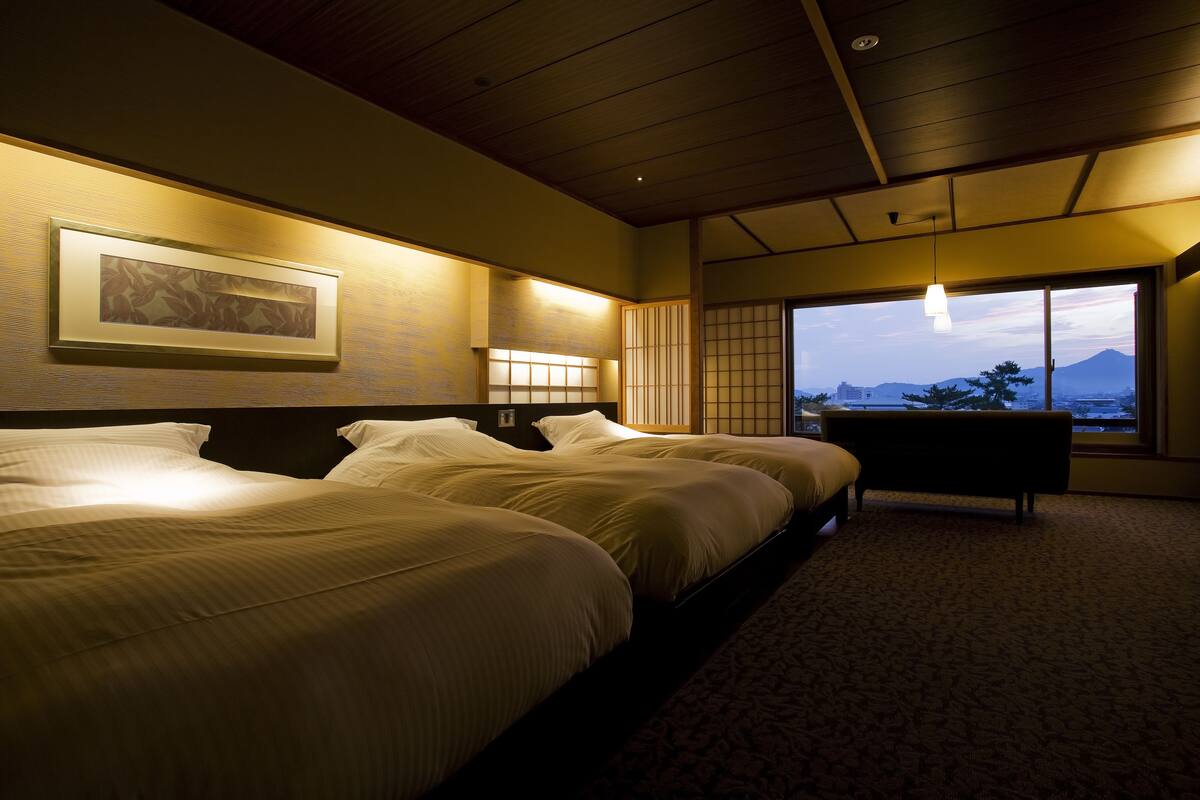 Een hotelkamer met twee bedden, een groot raam met uitzicht op een berg en een traditionele Japanse schuifdeur.