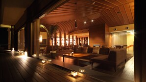 Un espacio interior amplio con piso de madera, un conjunto de sofás y un gran ventanal con vista a un jardín.