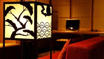 A room with a traditional Japanese-style partition featuring a tree and wave design, a red sofa, and a television in the background.