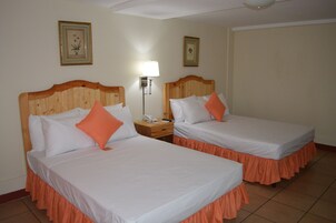 Dos camas individuales con cabeceros de madera, ropa de cama blanca y faldas naranjas. Hay una mesita de noche con un teléfono y una lámpara entre las camas.
