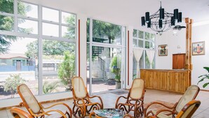 A room with large windows, wicker chairs, a wooden reception desk, and a chandelier. - Hotel la Estación Granada (Granada)