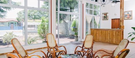 A room with large windows, wicker chairs, a wooden reception desk, and a chandelier.