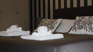 A neatly made bed with rolled white towels and floral-patterned pillows. - Hotel Trieste Catania (Catania)