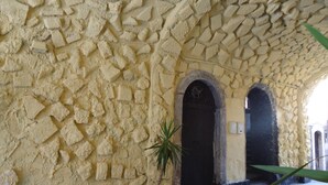 A stone wall with a textured pattern, a potted plant, and two dark arched doors. - Hotel Trieste Catania (Catania)