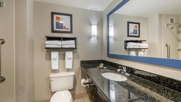 A modern bathroom with a toilet, sink, and shower. There are towels on a shelf and a framed picture on the wall.