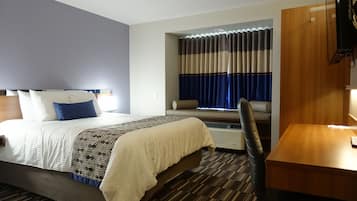 A hotel room with a bed, a desk, a chair, a window with curtains, and a television.