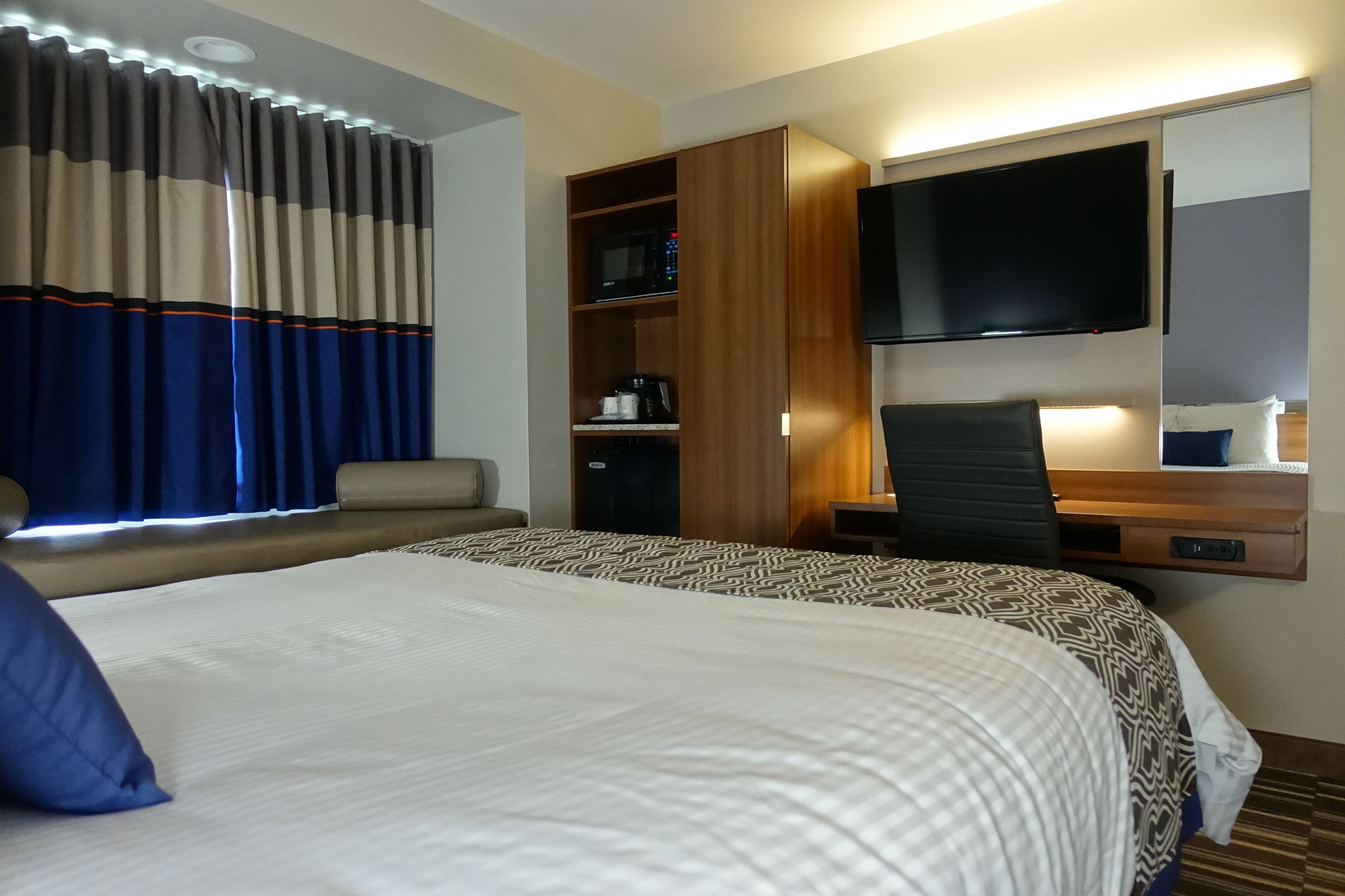 Ein Hotelzimmer mit einem großen Bett, einem Schreibtisch, einem Flachbildfernseher, einer Mikrowelle und einer Kaffeemaschine.
