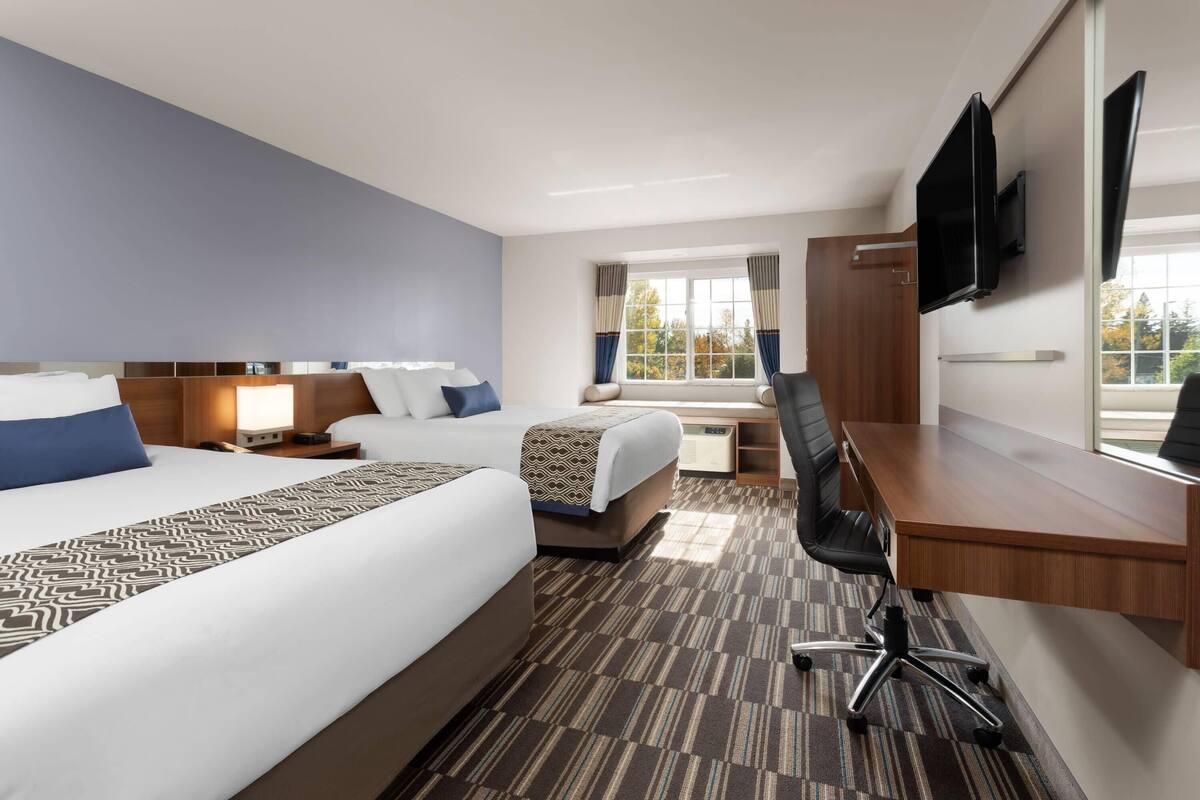 A hotel room with a large bed, a desk, a chair, a TV, and a window with curtains.