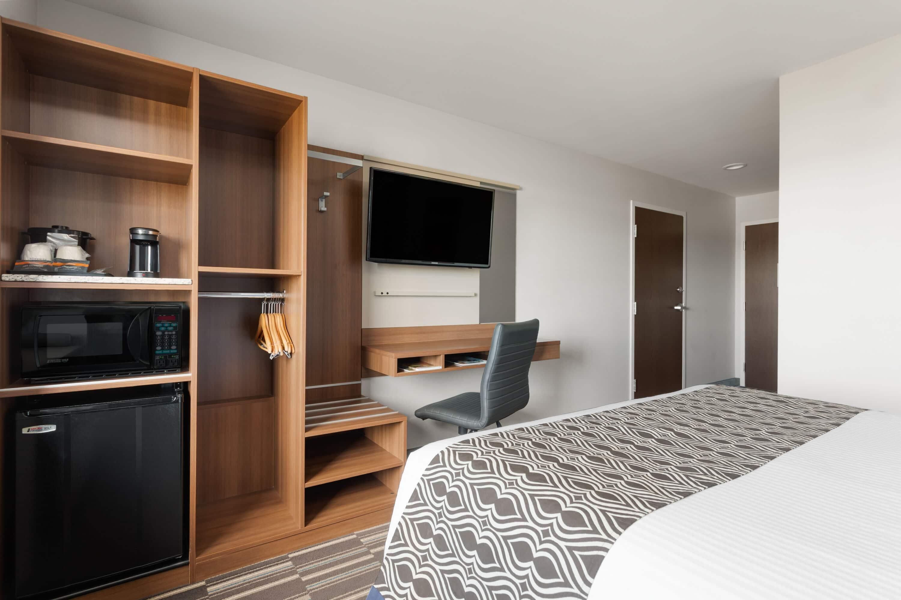 Habitación de hotel con cama, escritorio con silla, televisor, armario y un refrigerador pequeño.