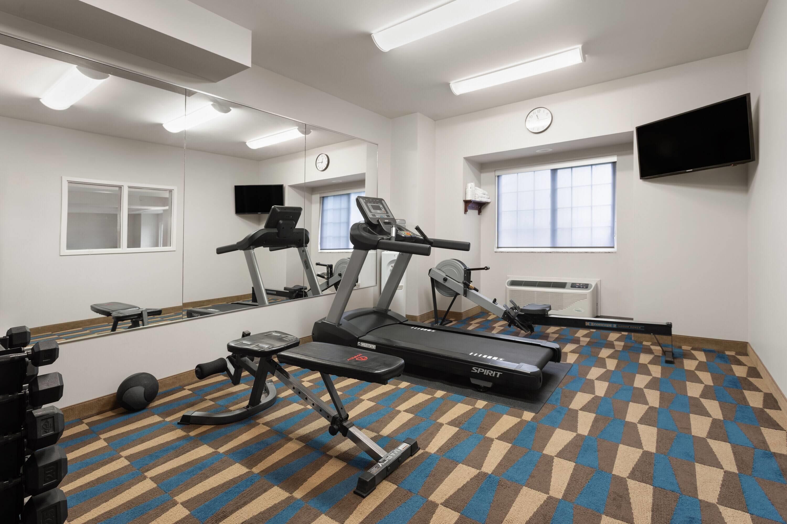 Une salle de sport équipée de tapis de course, d’un banc et d’un mur recouvert de miroirs.