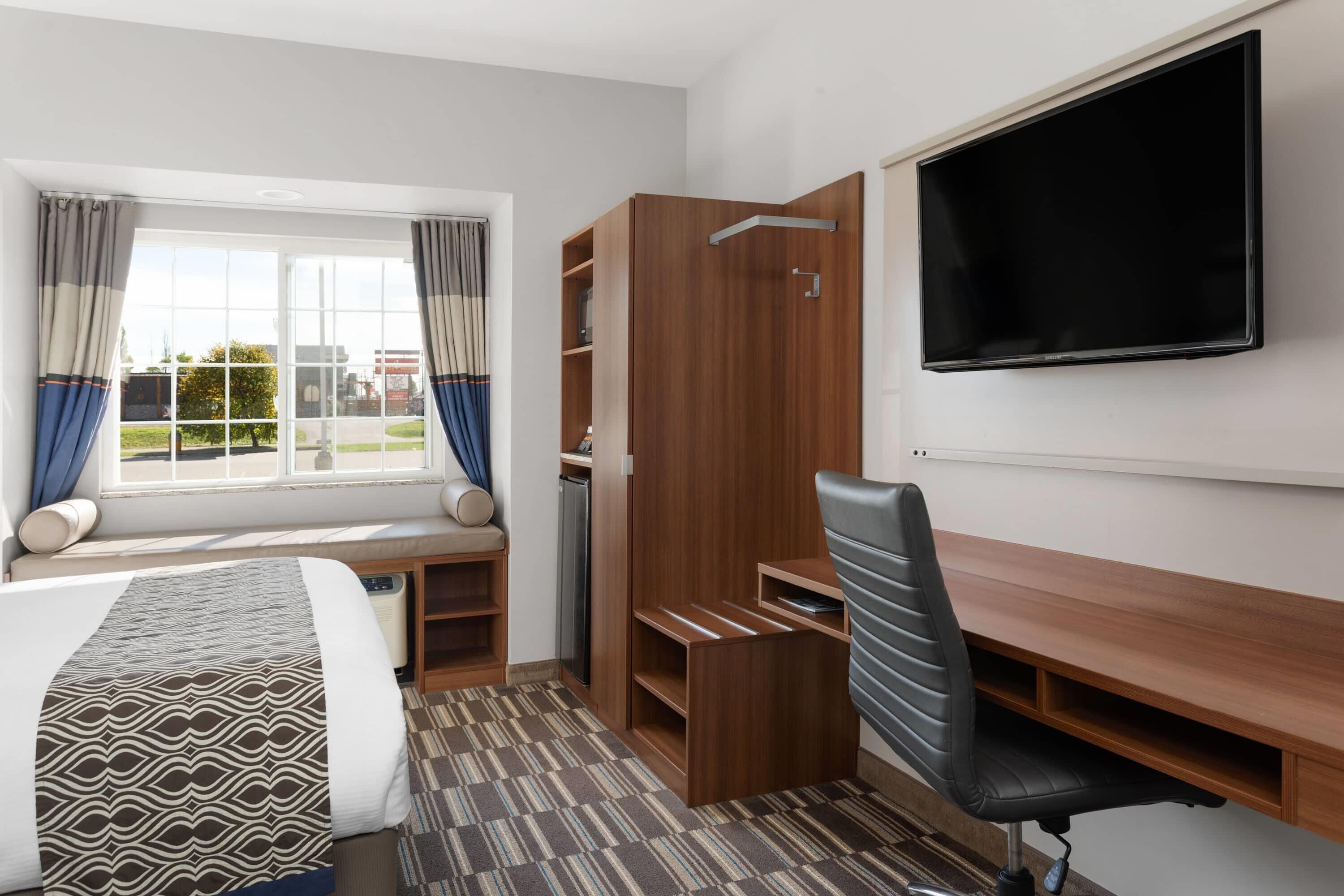 A hotel room with a bed, a desk, a chair, a TV, and a wardrobe.