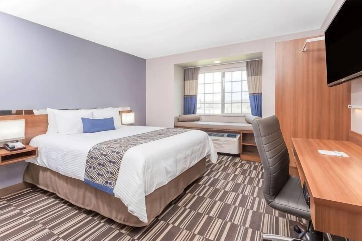 A hotel room with a bed, desk, chair, television, and window.