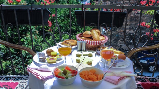 A table set with food and drinks, surrounded by a garden with red flowers and a metal fence. - Hotel Pansion Stari Grad - Sarajevo (Sarajevo)