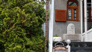 A building facade with a stone wall, a wooden door with a lattice design, and a metal gate with a decorative emblem. - Hotel Pansion Stari Grad - Sarajevo (Sarajevo)