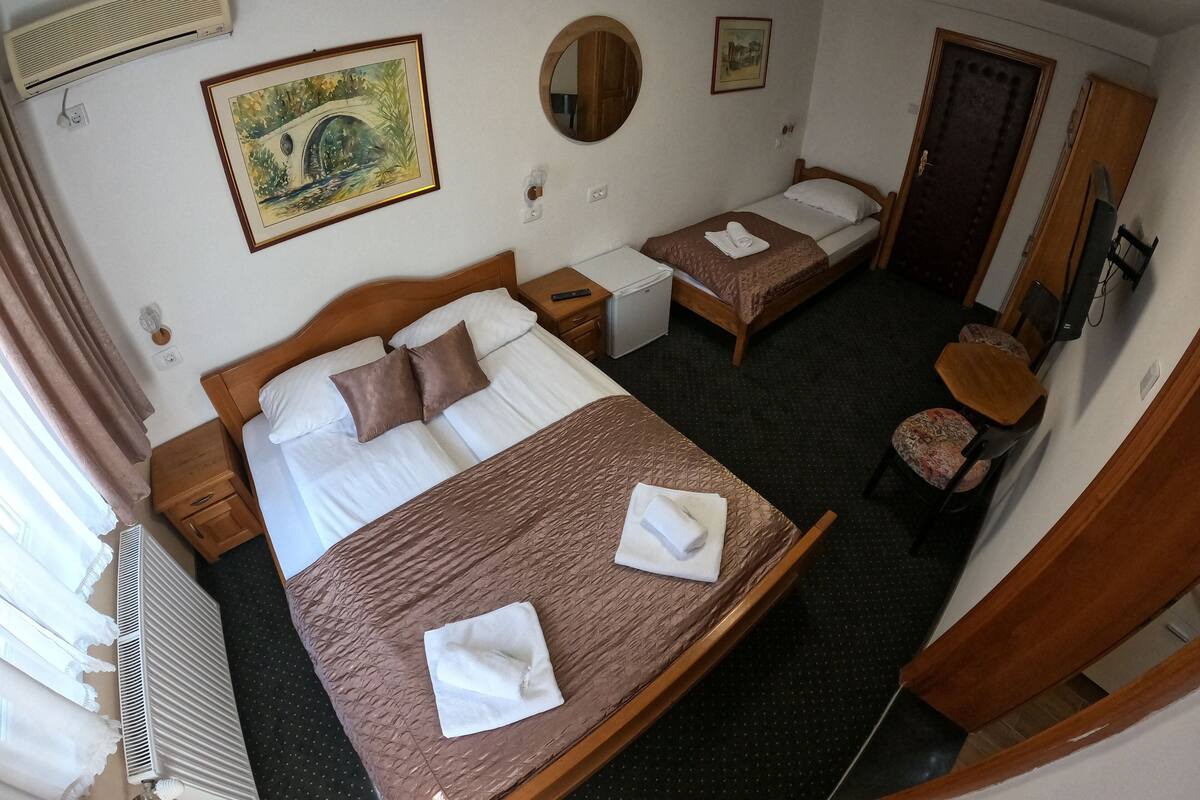 A hotel room with a large bed, a smaller bed, a desk, a chair, a mirror, and a painting on the wall.