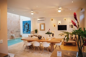 A modern living room with a dining area, a pool, and a large artwork on the wall.