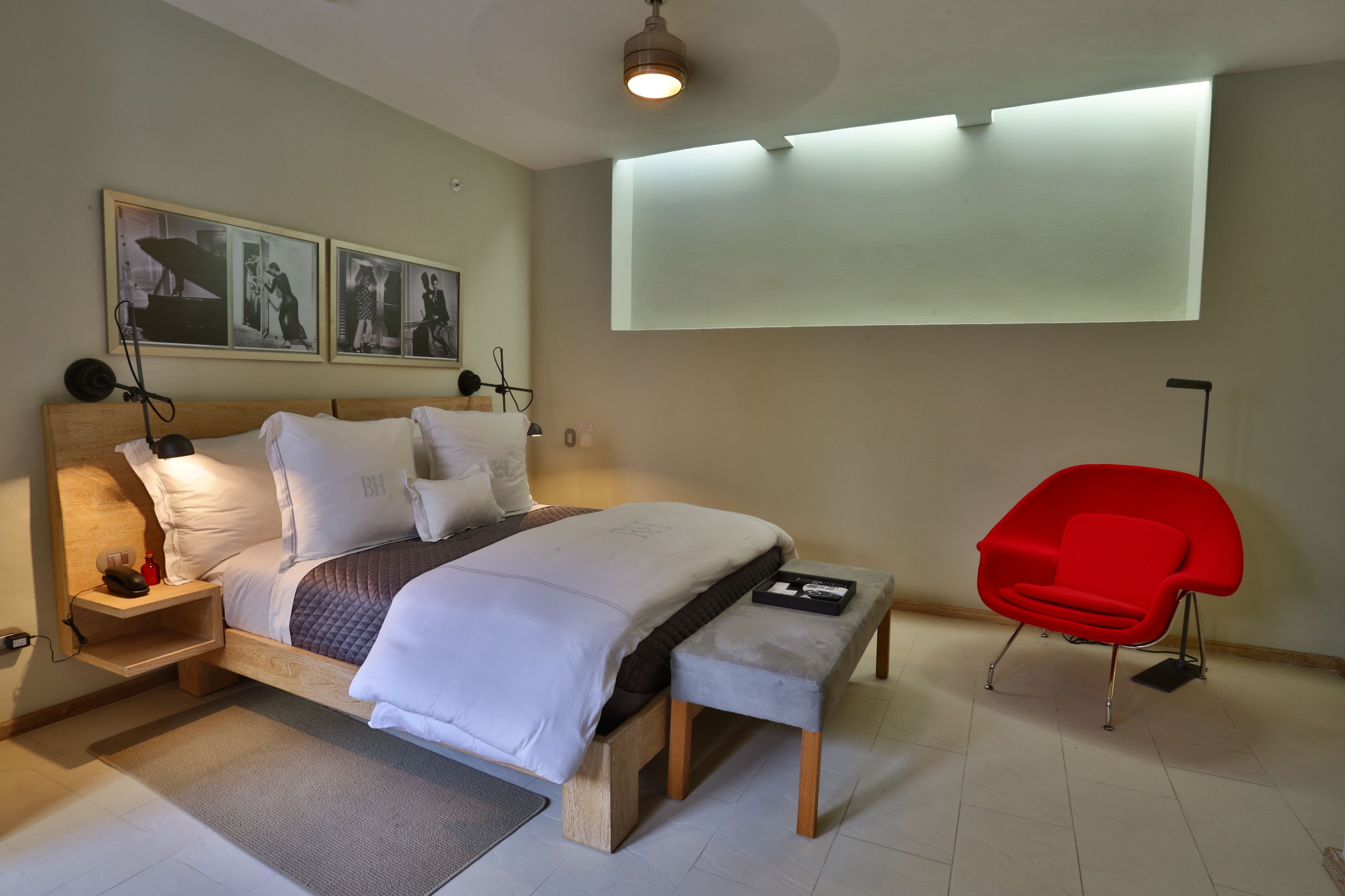 A modern bedroom with a bed, bedside tables, a red chair, and wall-mounted artwork.