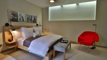 A modern bedroom with a bed, bedside tables, a red chair, and wall-mounted artwork.