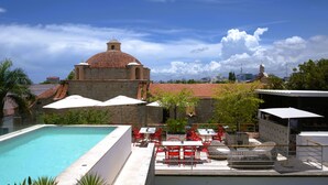 A rooftop pool area with a stone building in the background, red chairs, and umbrellas. - Billini Hotel, Historic Luxury (Santo Domingo)