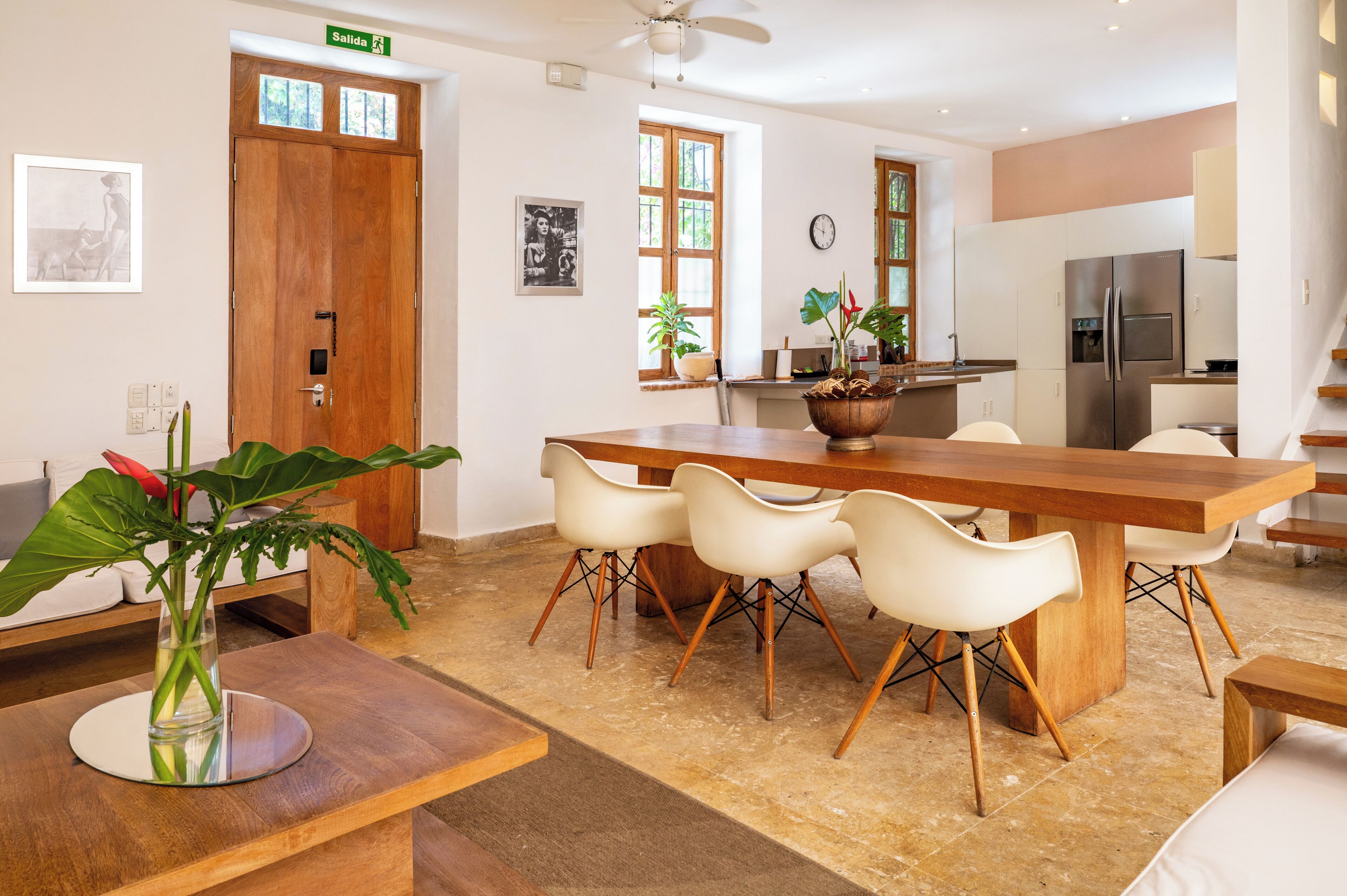A modern kitchen with a wooden dining table, white chairs, and a refrigerator.
