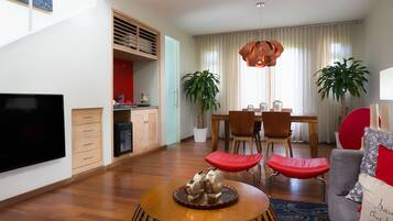 A modern living room with a flat-screen TV, wooden coffee table, red cushioned seating, and a dining area with a wooden table and chairs.