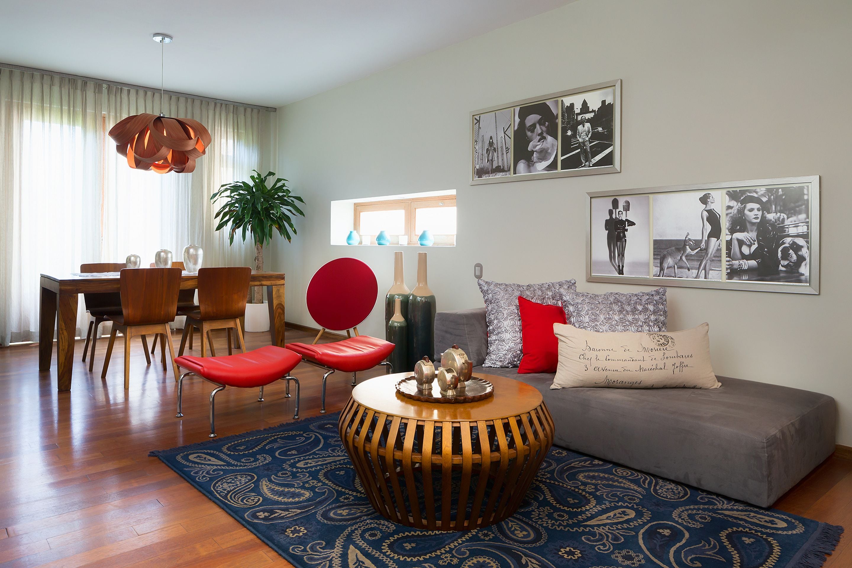 Una sala de estar moderna con comedor, que presenta una mesa de centro redonda de madera, un sofá gris, sillas rojas y un tapete azul con diseño.