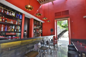 A bar area with shelves of liquor bottles, hanging pendant lights, and seating.
