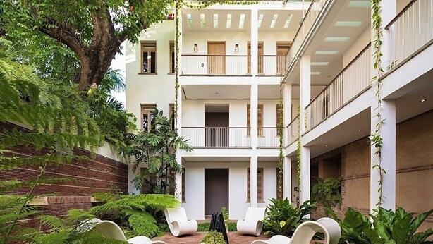 A multi-level building with a courtyard featuring white chairs, potted plants, and a tree. - Billini Hotel, Historic Luxury (Santo Domingo)