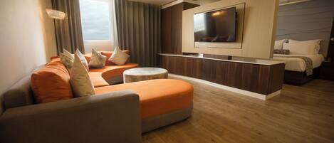 Ein modernes Hotelzimmer mit einer Couch, einem Hocker und einem Flachbildfernseher, der an einem Holzpaneel befestigt ist.