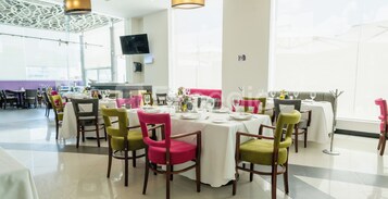 Un restaurante con varias mesas dispuestas para comer, sillas con cojines y un televisor en la pared.