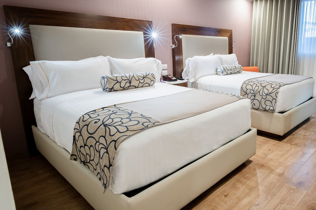 Habitación de hotel con dos camas, suelo de madera y vistas al exterior a través de cortinas.