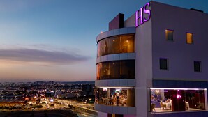 Een modern hotel met een opvallend ‘HS’ logo, grote ramen en uitzicht op de skyline.