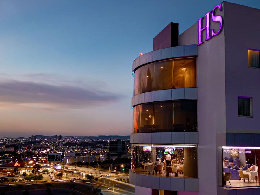 Un hotel moderno con un llamativo letrero 'HS', grandes ventanales y vistas a la ciudad.