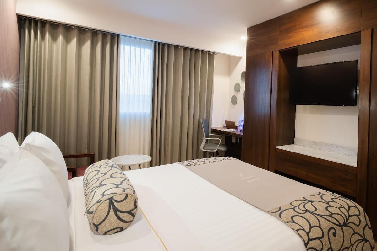 Habitación de hotel con cama, escritorio, silla, televisor y cortinas.