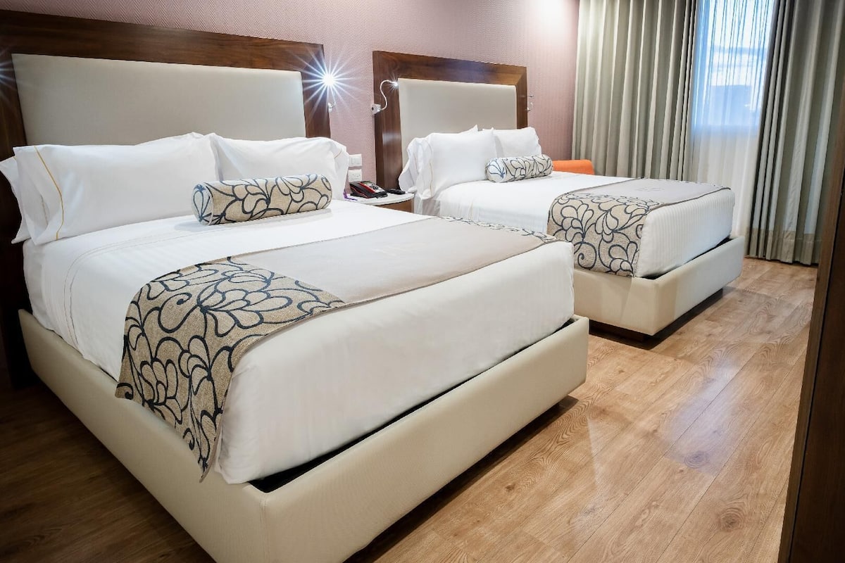 Habitación de hotel con dos camas, piso de madera y vista al exterior a través de la ventana.