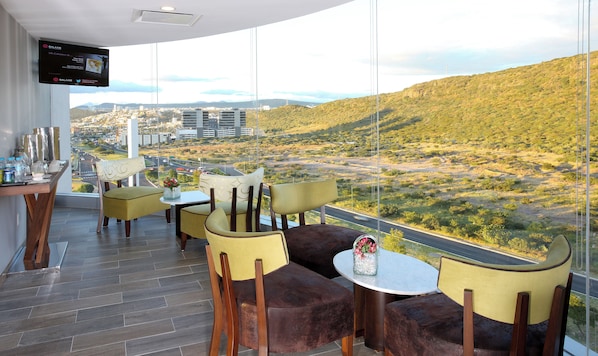 A modern dining area with a city view, featuring a flat-screen TV, comfortable seating, and a table with amenities. - HS HOTSSON Hotel Querétaro (Querétaro)