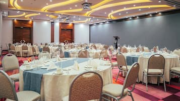 A banquet hall with round tables, chairs, and a stage.