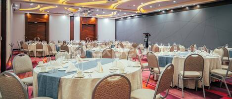 Un salón de banquetes con mesas redondas, sillas y un escenario.