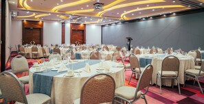 Een feestzaal met ronde tafels, stoelen en een podium.
