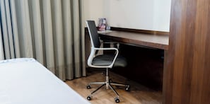 Una habitación de hotel con cama, un escritorio con silla y una ventana con cortinas.