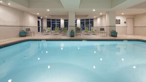 Une piscine intérieure dotée de nombreuses chaises longues et offrant une vue dégagée sur l’ensemble de l’espace piscine.