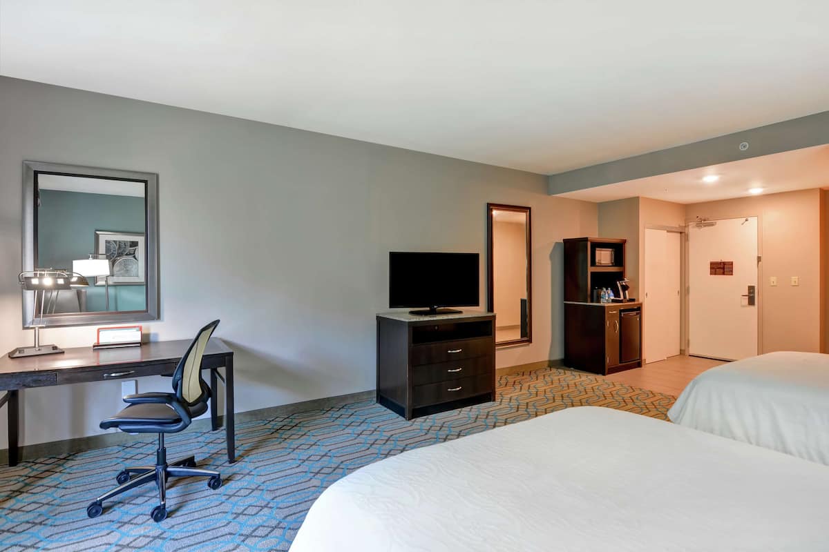 A hotel room with a bed, a desk with a chair, a television, a wardrobe, and a bathroom visible through an open door.