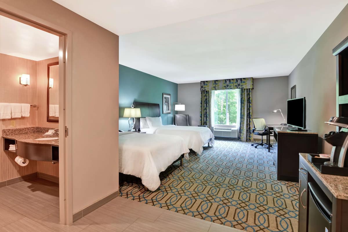 A hotel room with a bathroom, two beds, a desk, and a television.
