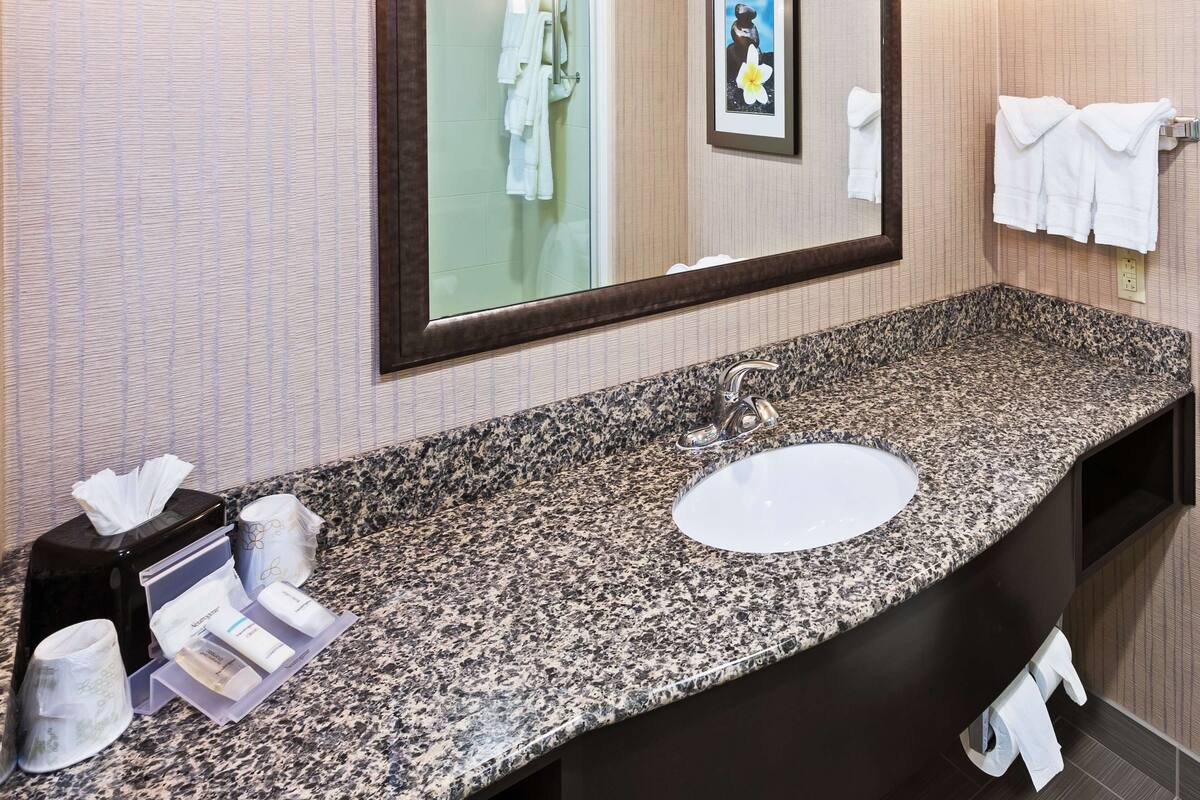 A hotel bathroom with a granite countertop, a sink, and a large mirror.