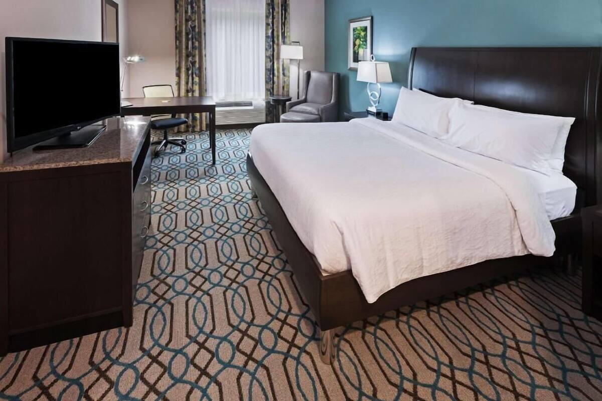 A hotel room with a bed, desk, TV, and a view of the outdoors.